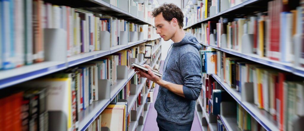 Male student reading book in library