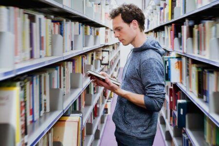 Male student reading book in library