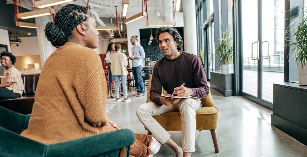 Man writing on notepad while talking to colleague 1