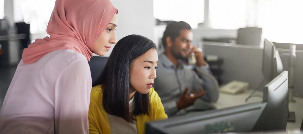 Two women working together in office at computer