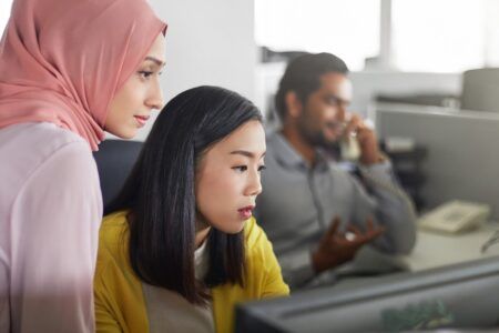 Two women working together in office at computer